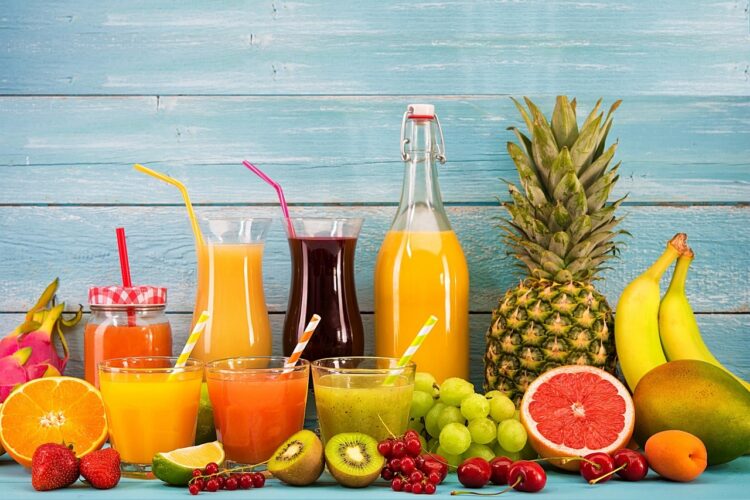 Bottles and glasses of fresh juice with a collection of fruits arranged around them
